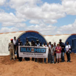 People holding a BLU-MED Response Systems sign in Haiti in front of a mobile field hospital