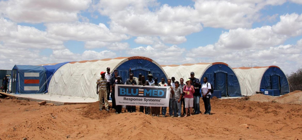 Group of people around a 'Blu-Med' sign in front of Blu-Med structures